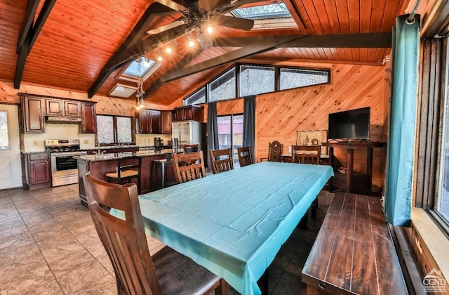 dining space featuring wood walls, vaulted ceiling with skylight, ceiling fan, and wood ceiling