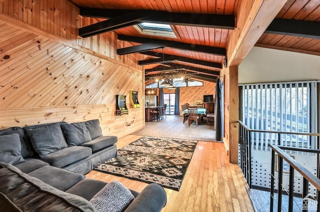 living room with light hardwood / wood-style floors, wood walls, vaulted ceiling with skylight, and wooden ceiling