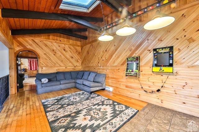 living room with hardwood / wood-style floors, wood walls, high vaulted ceiling, a skylight, and beam ceiling