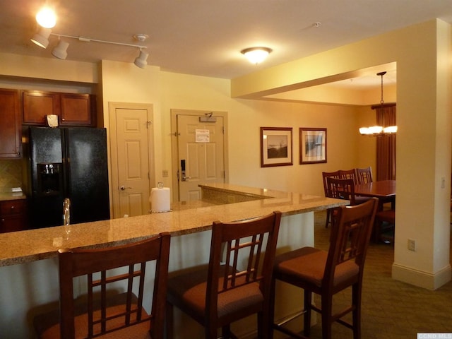 kitchen with a kitchen bar, black fridge with ice dispenser, an inviting chandelier, and hanging light fixtures