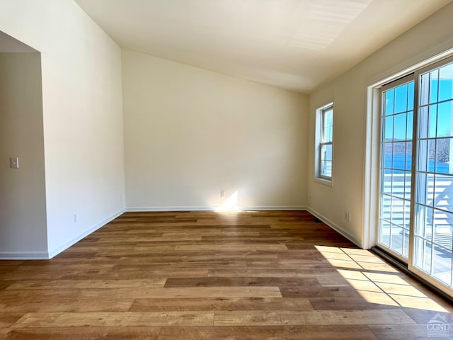 empty room with baseboards, wood finished floors, and vaulted ceiling