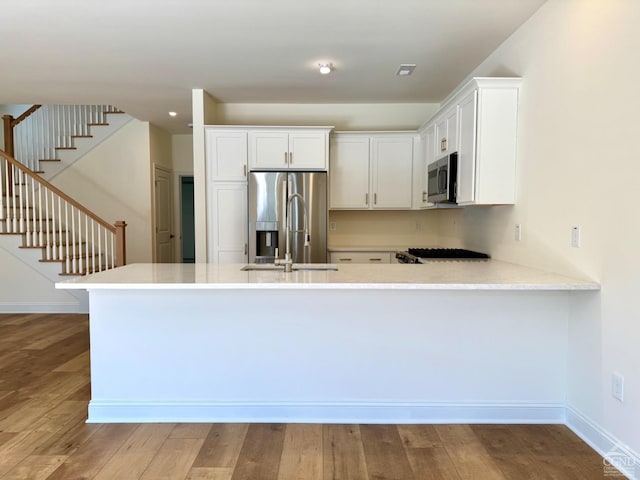 kitchen featuring wood finished floors, light countertops, a peninsula, stainless steel appliances, and white cabinetry