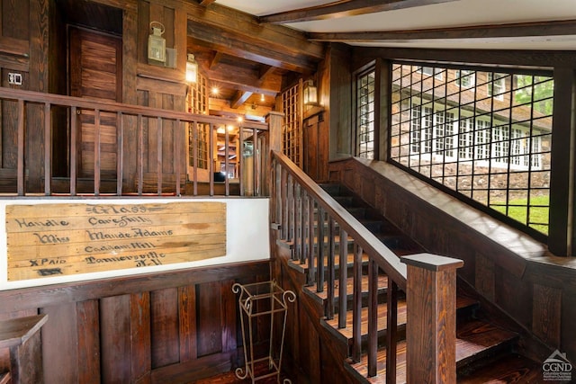 stairway with beam ceiling, a wealth of natural light, and wood walls