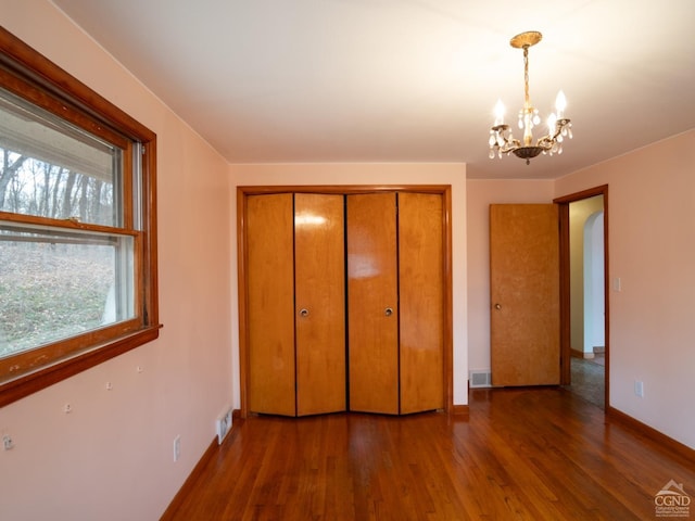 unfurnished bedroom with dark wood-type flooring, a closet, and a chandelier