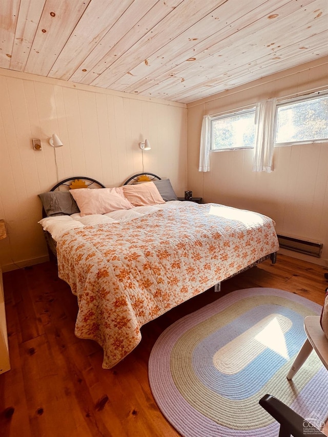 bedroom with wood ceiling, wooden walls, dark wood-type flooring, and a baseboard heating unit