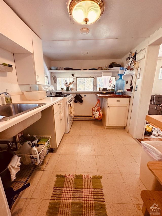 kitchen with white gas range, white cabinetry, and sink