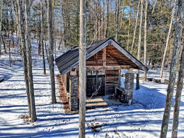 snow covered structure featuring an outdoor structure and a wooded view