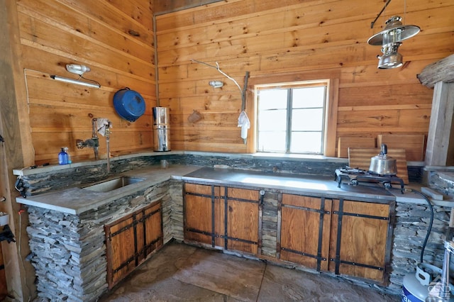 interior space with a sink, brown cabinets, wood walls, and hanging light fixtures