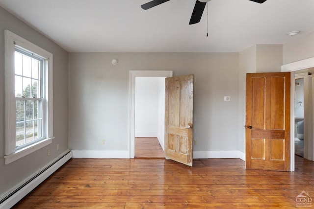 empty room featuring light wood-style floors, a baseboard radiator, and baseboards