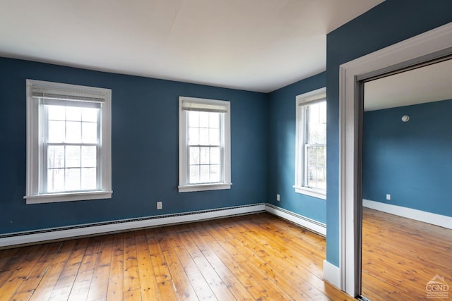 empty room featuring hardwood / wood-style flooring, a baseboard radiator, and plenty of natural light