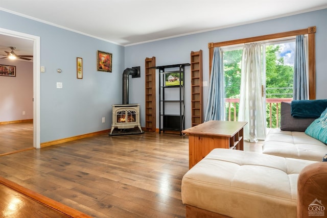 living room featuring light hardwood / wood-style flooring, a wood stove, ceiling fan, and crown molding