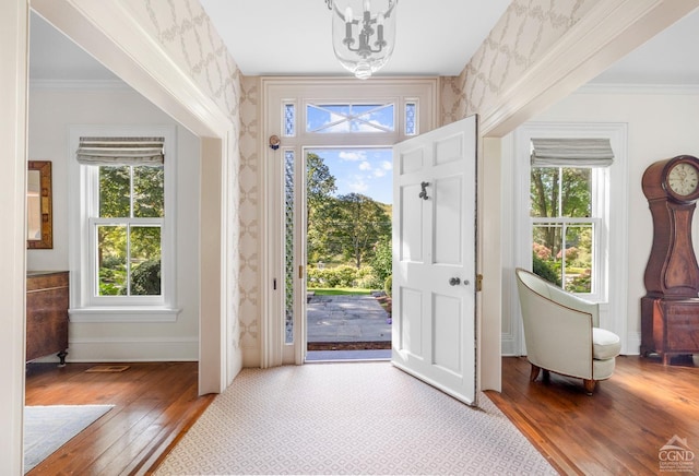 entryway with a wealth of natural light, crown molding, wood-type flooring, and an inviting chandelier