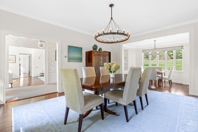 dining area with wood-type flooring, ornamental molding, and a notable chandelier