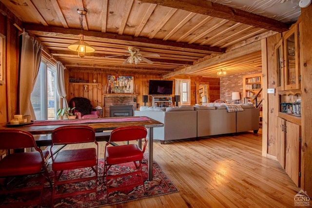 dining room with wooden walls, beamed ceiling, light wood finished floors, and ceiling fan