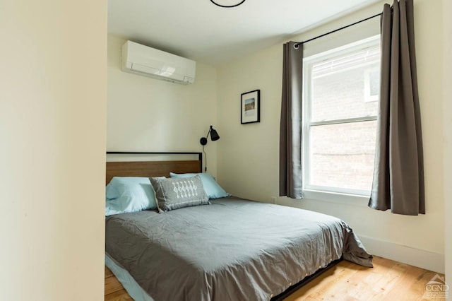 bedroom featuring multiple windows, an AC wall unit, and wood finished floors