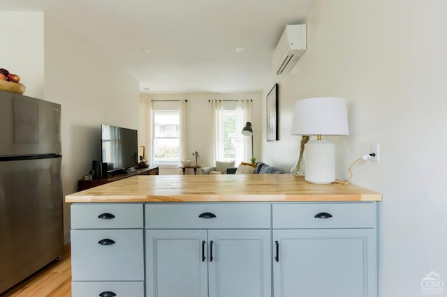 kitchen with a wall unit AC, freestanding refrigerator, open floor plan, light wood-style floors, and butcher block countertops