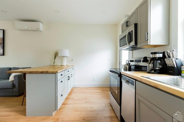 kitchen featuring appliances with stainless steel finishes, a kitchen breakfast bar, butcher block countertops, light wood-style flooring, and a wall mounted AC
