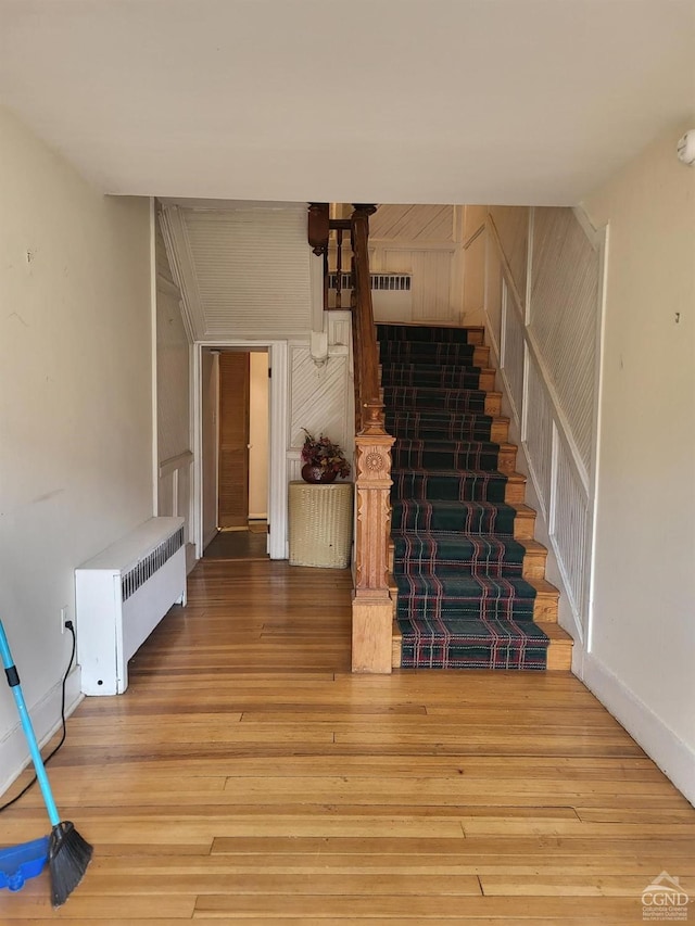 stairway with wood walls, radiator heating unit, and hardwood / wood-style floors