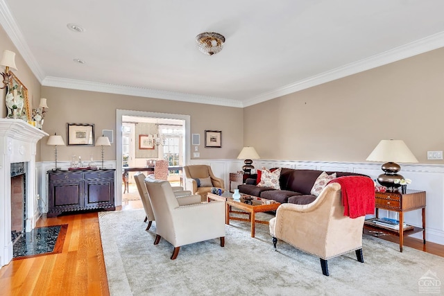 living area with crown molding, a fireplace, light wood finished floors, and wainscoting