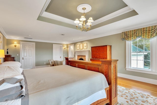 bedroom featuring a tray ceiling, crown molding, light wood finished floors, and a chandelier