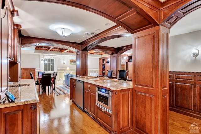 kitchen with stainless steel oven, light wood-style floors, arched walkways, and ornate columns