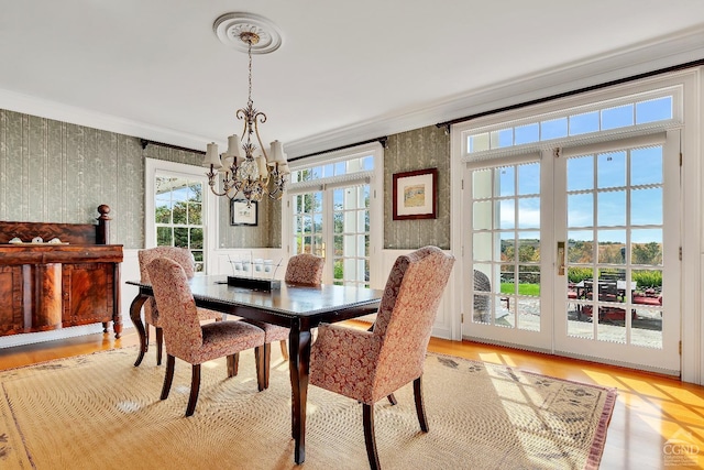 dining area with light wood finished floors, wallpapered walls, an inviting chandelier, and ornamental molding