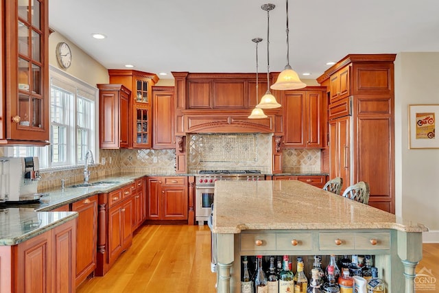 kitchen featuring a center island, light stone countertops, pendant lighting, light wood-style flooring, and stainless steel range