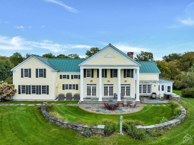 back of property with a chimney, metal roof, a yard, a patio area, and a standing seam roof