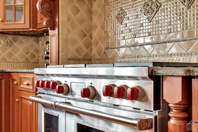 details with decorative backsplash, glass insert cabinets, range with two ovens, and brown cabinetry