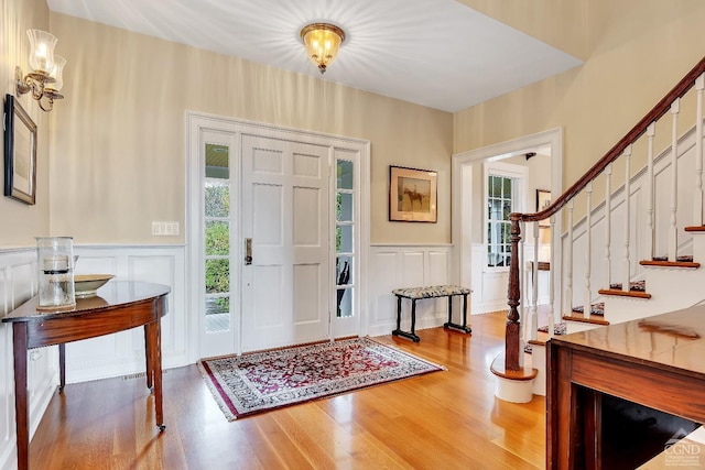 foyer entrance with stairs, a decorative wall, wood finished floors, and a wainscoted wall