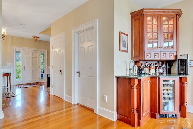 bar featuring light wood-type flooring, a sink, wine cooler, indoor wet bar, and baseboards