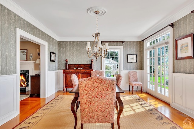 dining space with wood finished floors, a wainscoted wall, wallpapered walls, an inviting chandelier, and crown molding