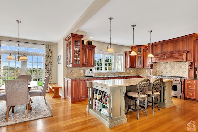 kitchen with light wood-type flooring, a sink, high end stainless steel range oven, a kitchen island, and backsplash