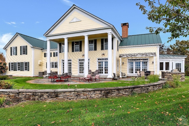 rear view of property with a standing seam roof, a lawn, a chimney, metal roof, and a patio