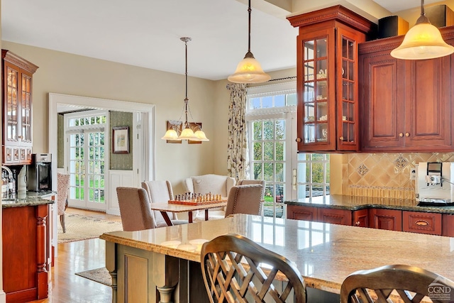 kitchen with a wainscoted wall, decorative light fixtures, backsplash, light stone countertops, and a chandelier