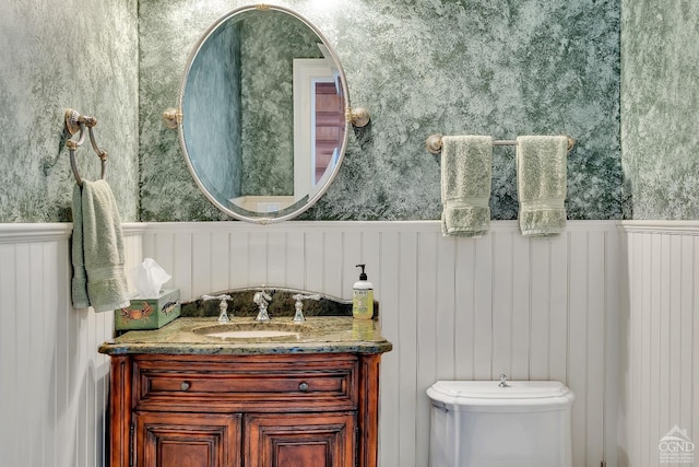 bathroom with vanity, wainscoting, and wallpapered walls