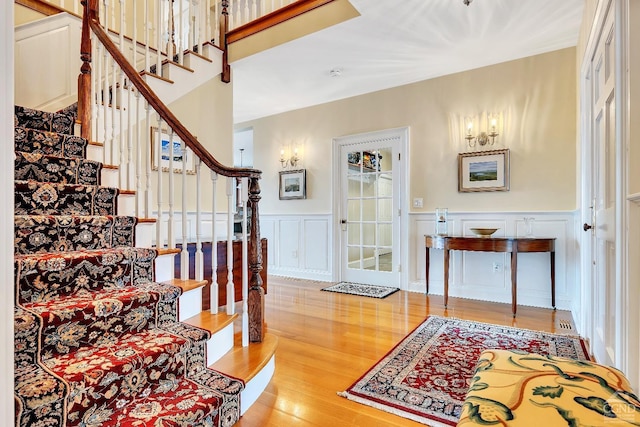 foyer entrance featuring light wood finished floors, a wainscoted wall, a decorative wall, and stairs