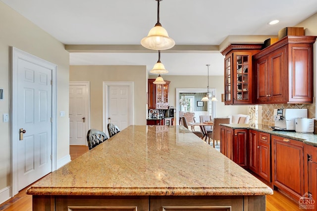 kitchen featuring light stone countertops, glass insert cabinets, light wood-type flooring, backsplash, and a center island