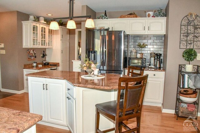 kitchen with glass insert cabinets, light wood finished floors, a kitchen island, and stainless steel fridge with ice dispenser