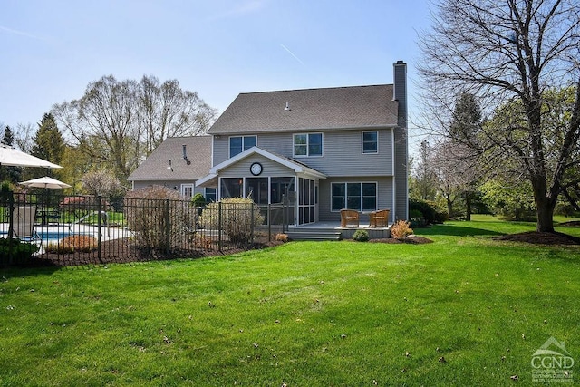 rear view of house with fence, a sunroom, a fenced in pool, a chimney, and a lawn