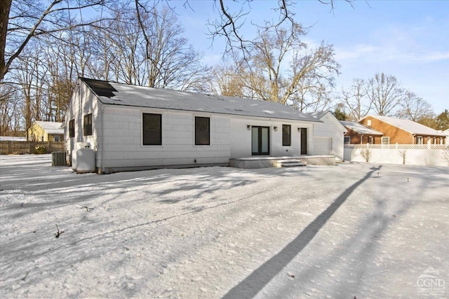 snow covered back of property featuring french doors, driveway, and fence