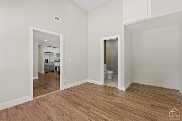 unfurnished bedroom with visible vents, wood finished floors, stainless steel fridge, and baseboards