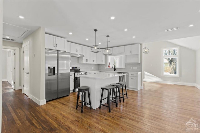 kitchen featuring visible vents, a kitchen island, stainless steel appliances, under cabinet range hood, and a kitchen breakfast bar