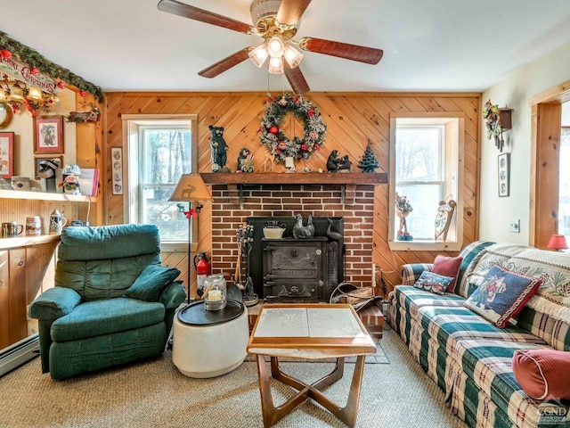 living room with a wood stove, wood walls, ceiling fan, and a baseboard heating unit