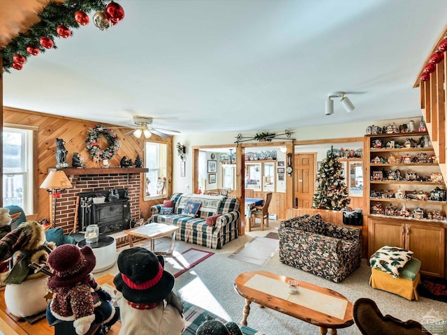 living room with ceiling fan, wood walls, a wood stove, and light carpet