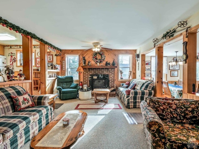 living room featuring ceiling fan with notable chandelier, light colored carpet, a wood stove, and wood walls