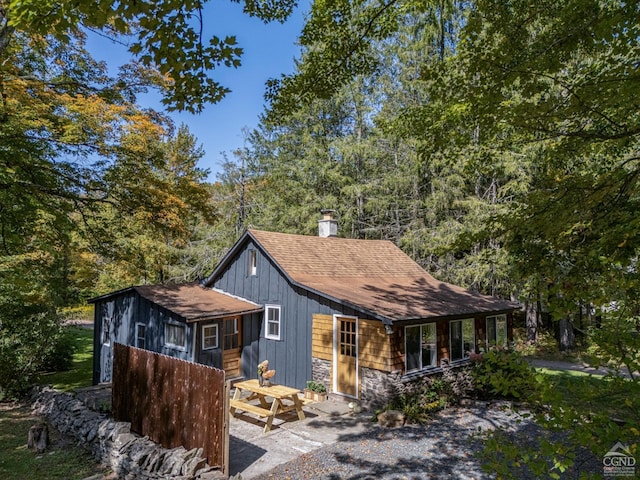 view of front of property featuring stone siding, roof with shingles, and a chimney