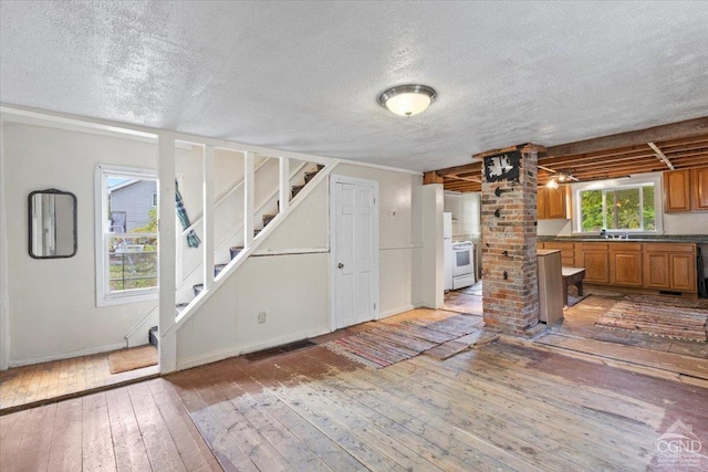 interior space featuring sink, white electric stove, decorative columns, wood-type flooring, and a textured ceiling