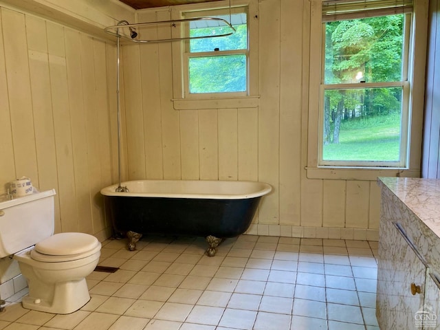 bathroom with a washtub, tile patterned floors, wooden walls, and toilet