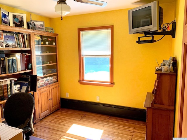 home office with baseboard heating, ceiling fan, and light hardwood / wood-style floors